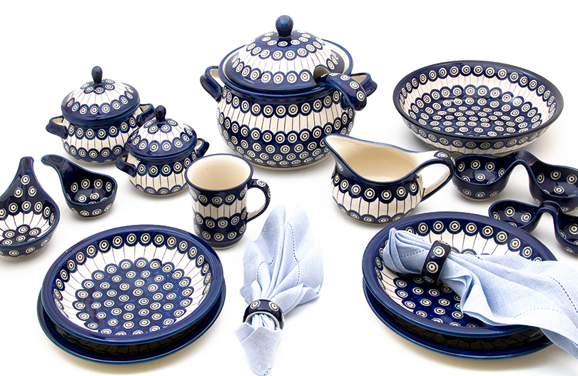 Various vessels such as plates, cups and mugs with handles with a pattern of peacock eyes stand side by side.